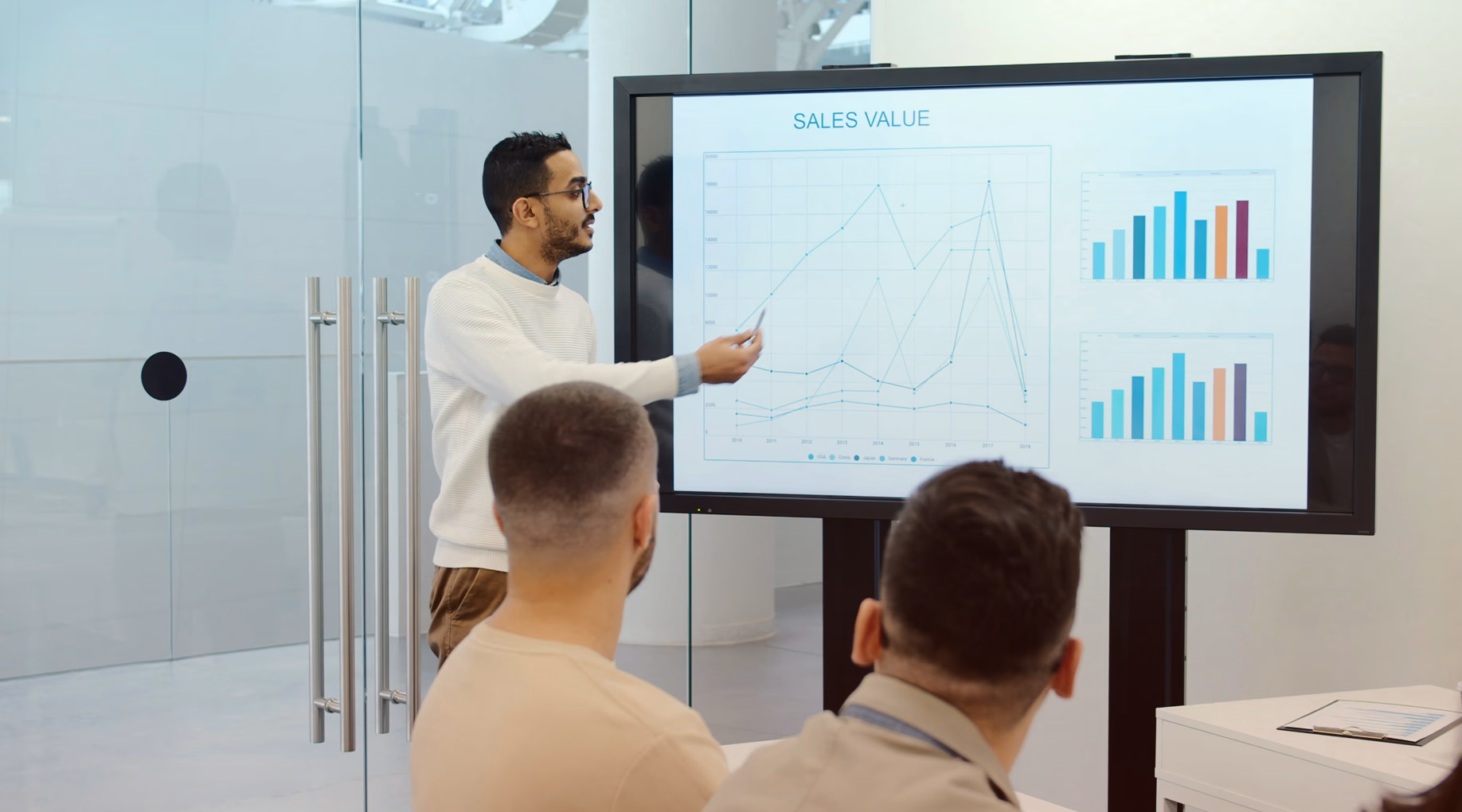 A presenter pointing at a sales chart on a wall screen
